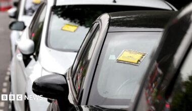 A generic-looking image shows a row of cars seen front-on with yellow and black Penalty Charge Notices affixed to their windscreens, on a road near Gatwick Airport in 2017.