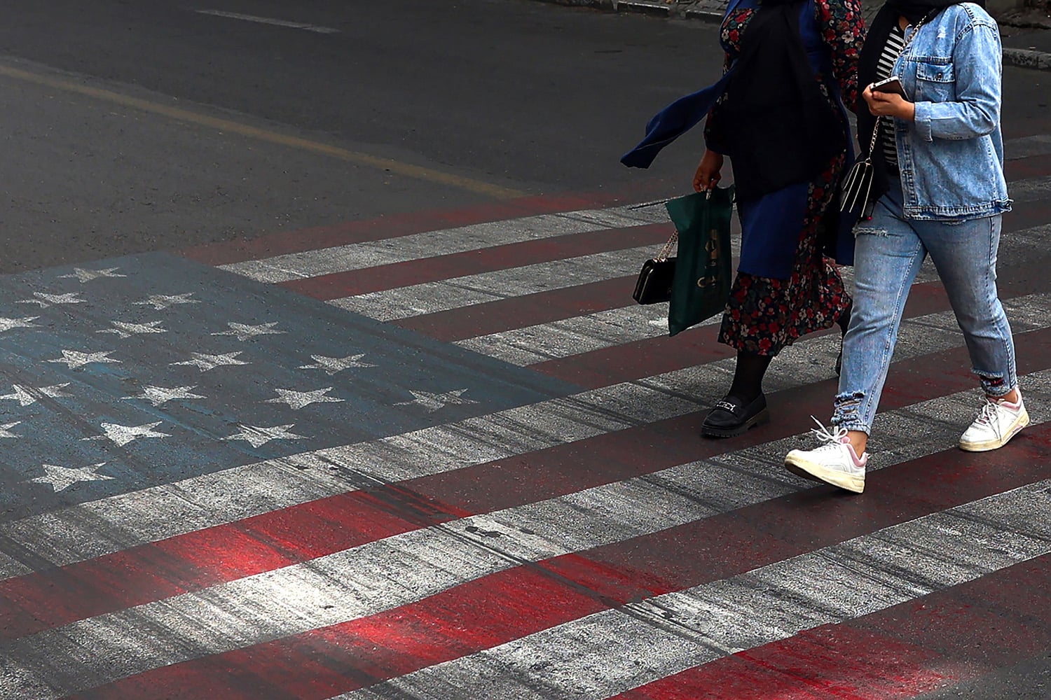 Two people walk across a pedestrian crosswalk painted to resemble an American flag. The shot is cropped so that their heads are cut out of the frame.