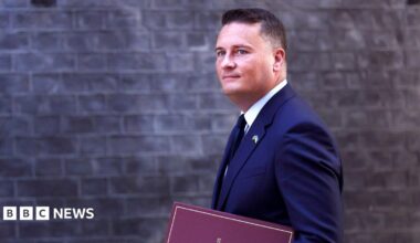 Wes Streeting walks in front of the Downing Street building facade carrying a binder that says 'Secretary of State for Defence' on the front, in September.