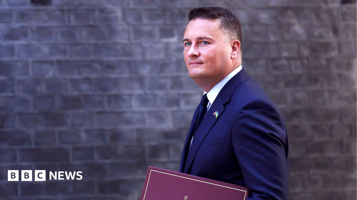 Wes Streeting walks in front of the Downing Street building facade carrying a binder that says 'Secretary of State for Defence' on the front, in September.