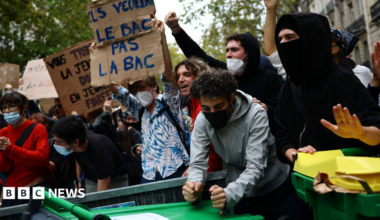 Protesters hold placards behind a barricade to block in Paris, 7 October