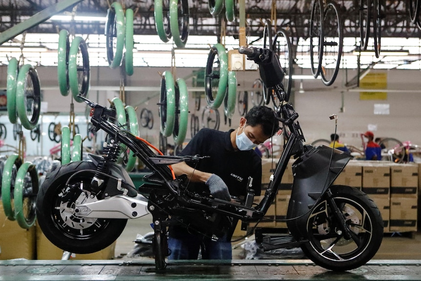 A man with a mask working on a motorbike ina factory setting
