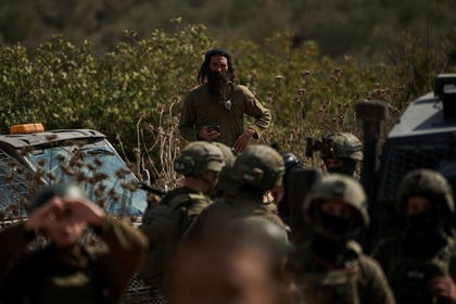 An Israeli settler overlooks members of Israeli forces blocking a road preventing Palestinians from reaching groves to harvest olives in the West Bank town of Turmus Ayya, Oct. 21, 2026.