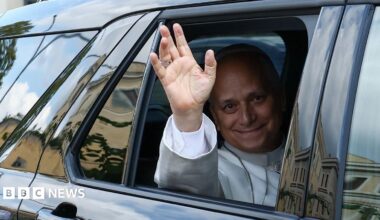 Pope Leo XIV waves from the window of a car as he leaves Rome's Gemelli University Hospital.