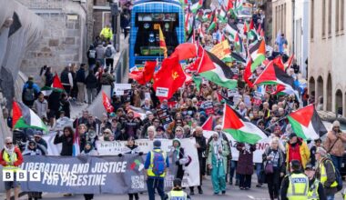 A crowd of people marching towards the Scottish Parliament in Edinburgh, waving Palestinian flags