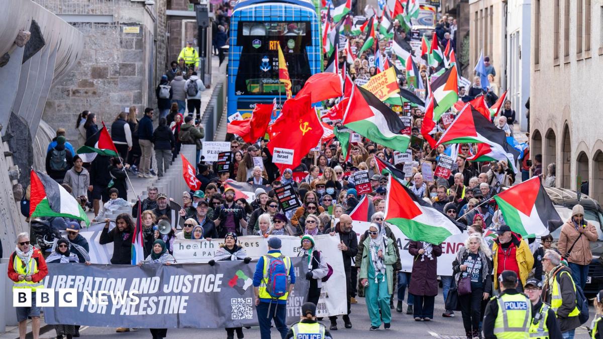 A crowd of people marching towards the Scottish Parliament in Edinburgh, waving Palestinian flags
