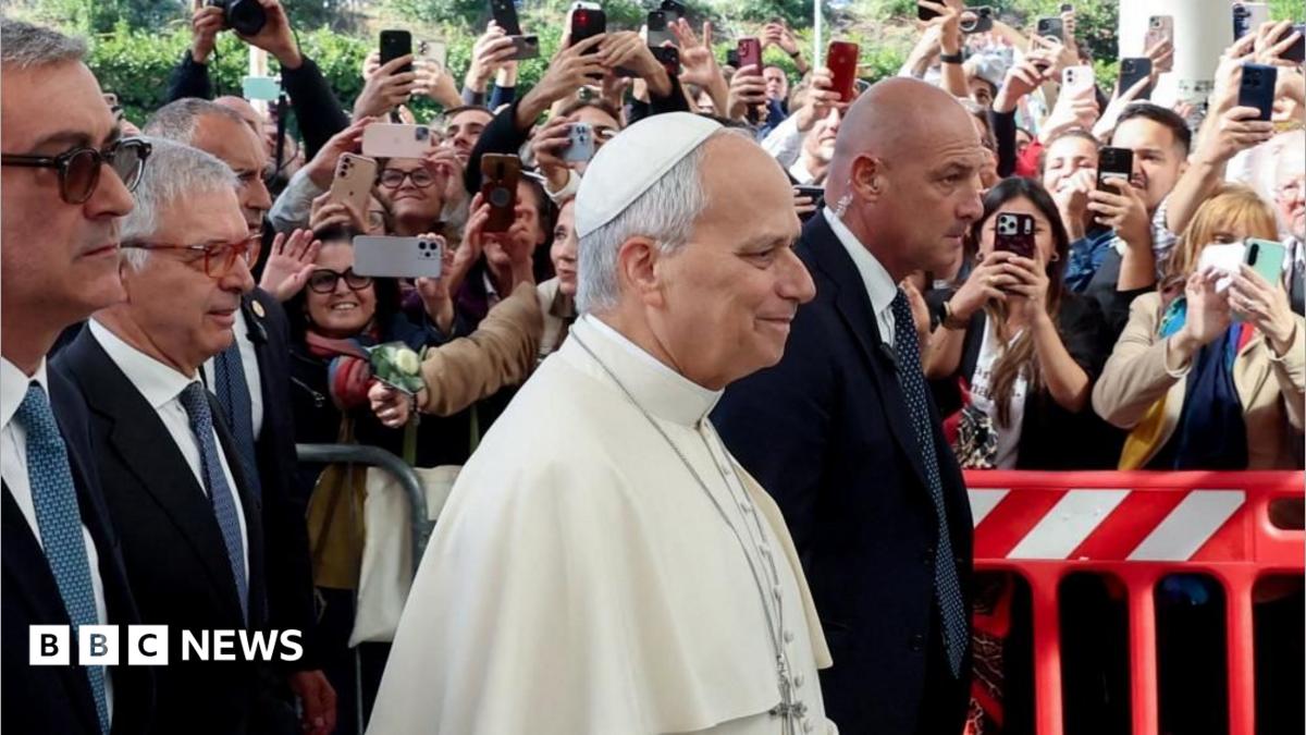 The Pope as he arrives at the hospital, with security following him and dozens of people behind barriers holding their phone up to catch a photo of him