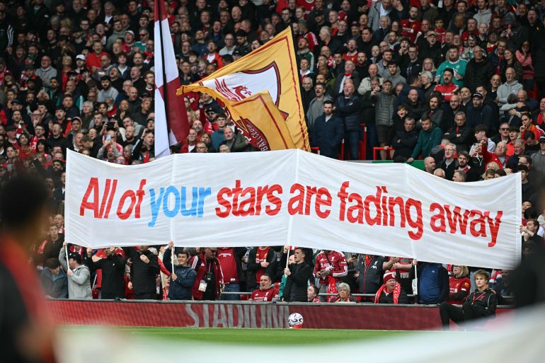 Liverpool fans hold up an banner mocking Manchester City's financial scandal as the television crew work pitch-side ahead of the English Premier League football match between Liverpool and Manchester City at Anfield in Liverpool, north west England on October 11, 2026. Manchester City face a hostile Anfield on Sunday when the Premier League leaders play bitter rivals Liverpool in their first game since being found guilty of breaking more than 100 financial rules. (Photo by Paul ELLIS / AFP) / RESTRICTED TO EDITORIAL USE. NO USE WITH UNAUTHORIZED AUDIO, VIDEO, DATA, FIXTURE LISTS, CLUB/LEAGUE LOGOS OR 'LIVE' SERVICES. ONLINE IN-MATCH USE LIMITED TO 120 IMAGES. AN ADDITIONAL 40 IMAGES MAY BE USED IN EXTRA TIME. NO VIDEO EMULATION. SOCIAL MEDIA IN-MATCH USE LIMITED TO 120 IMAGES. AN ADDITIONAL 40 IMAGES MAY BE USED IN EXTRA TIME. NO USE IN BETTING PUBLICATIONS, GAMES OR SINGLE CLUB/LEAGUE/PLAYER PUBLICATIONS. /