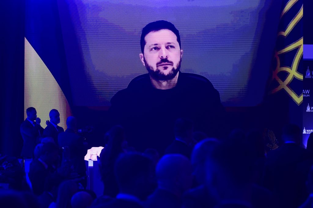 People watch Ukrainian President Volodymyr Zelenskyy on a large screen as he speaks to the Warsaw Security Forum in Warsaw, Poland, Monday, Oct. 12, 2026. (AP Photo/Attila Husejnow)
