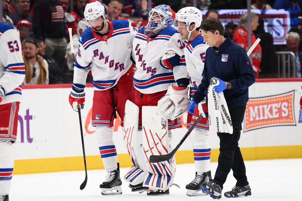 New York Rangers goaltender Igor Shesterkin is helped off the ice by teammates and a trainer.