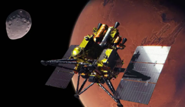 An artist&rsquo;s concept of JAXA&rsquo;s gold-foiled Martian Moons eXploration (MMX) spacecraft at Mars with an odd-shaped moon in the background.