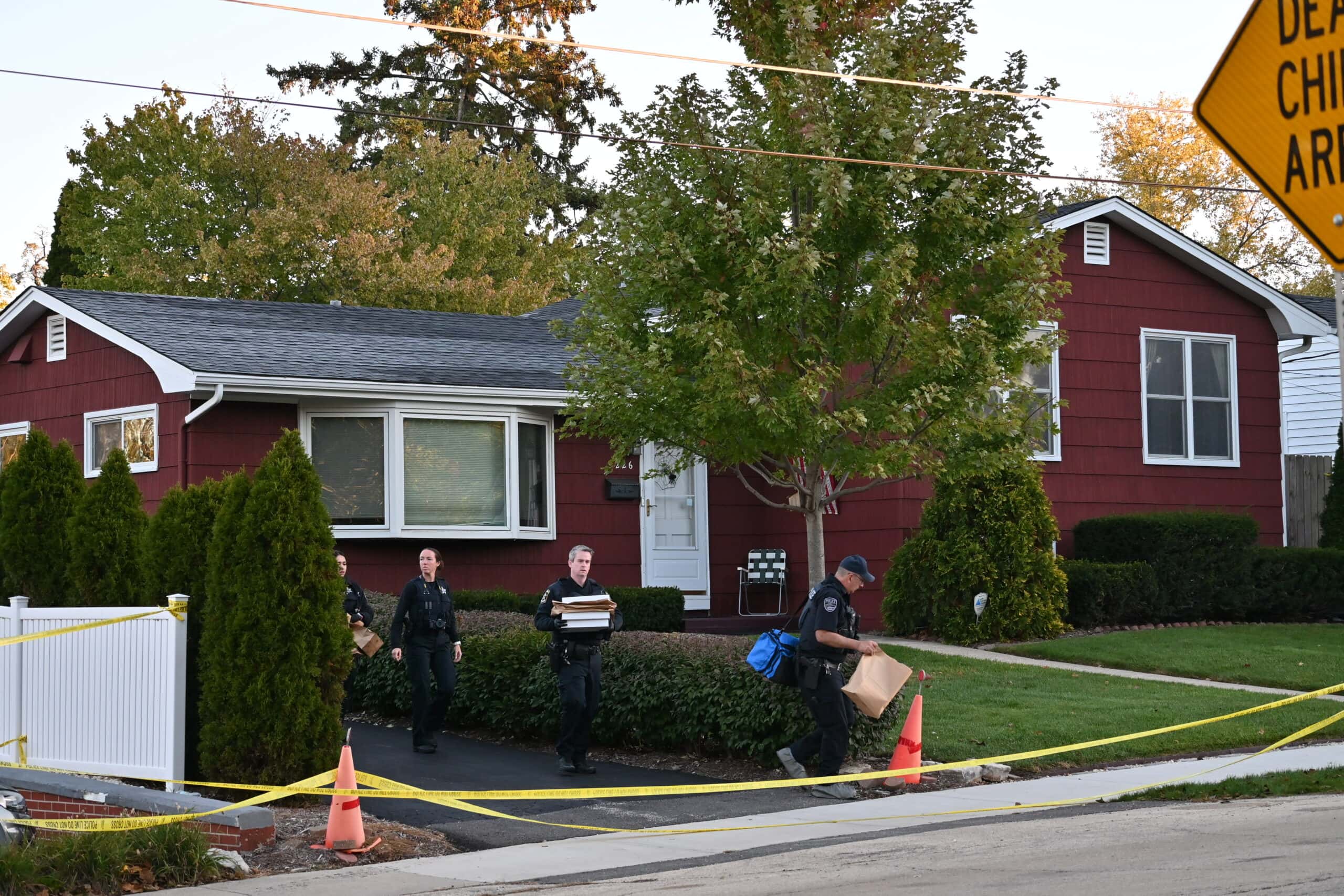 Investigators carry bags and boxes out of a red house surrounded by crime scene tape on Wellington Avenue in Mundelein