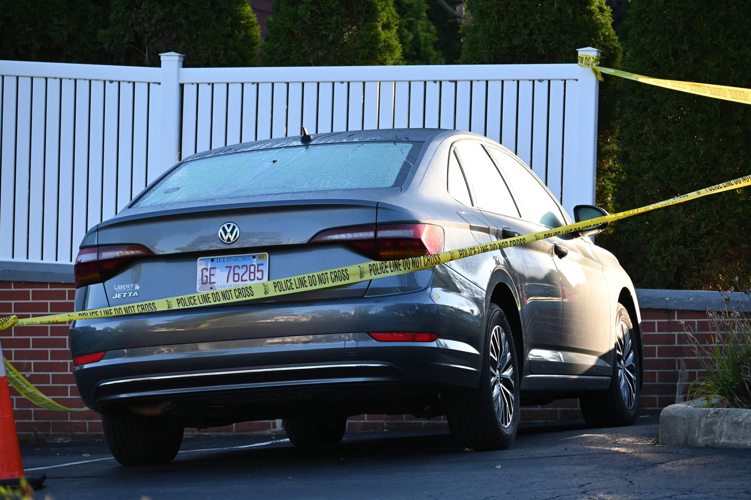 Crime scene tape wrapped around a gray Volkswagen Jetta in a parking lot