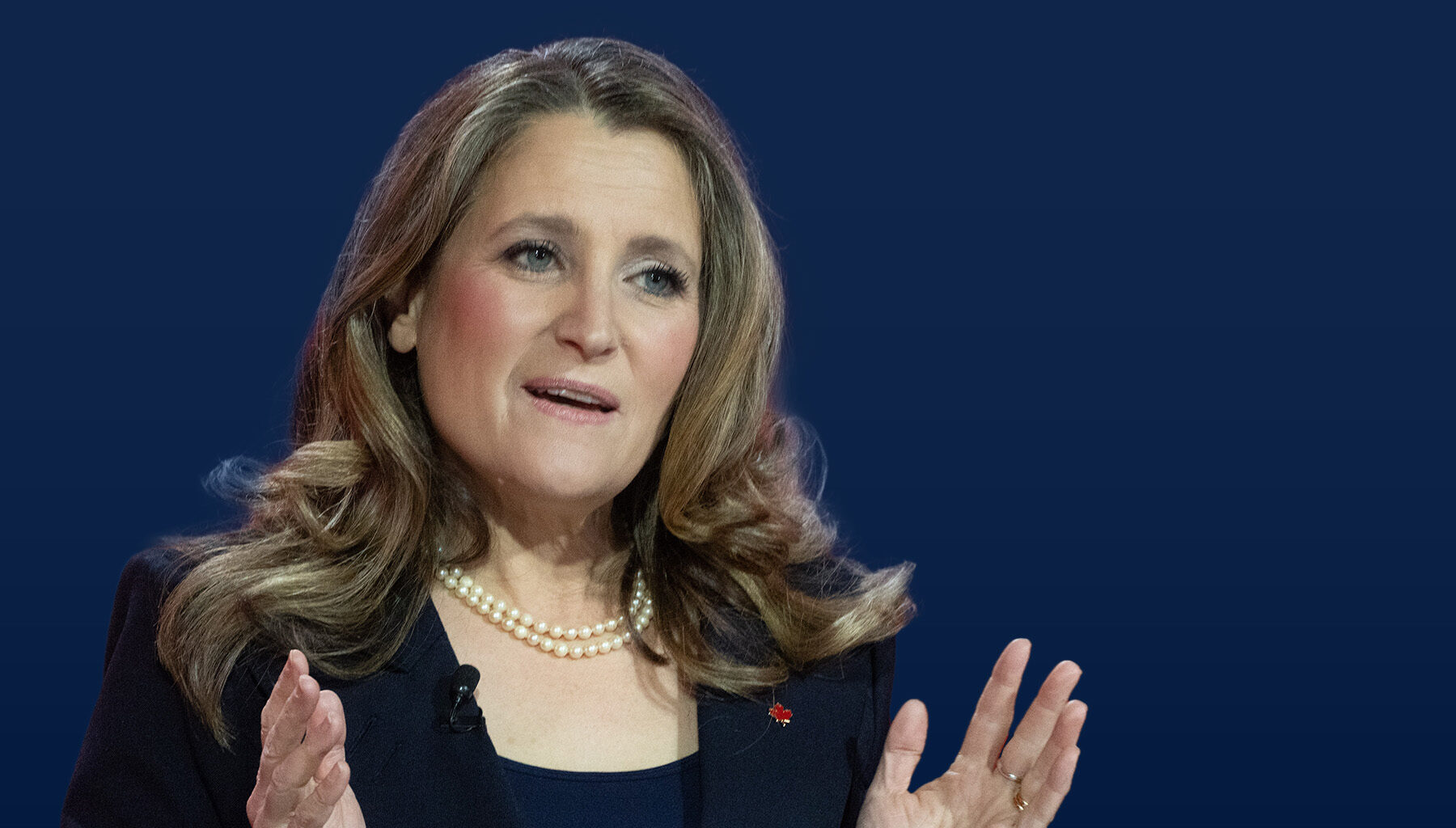Photo of Chrystia Freeland, a blond woman in a black blouse, speaking in front of a dark blue background.