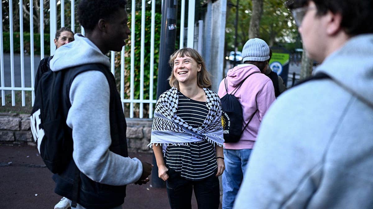 Greta Thunberg smiles while speaking with students outside a school in Saint-Denis, France