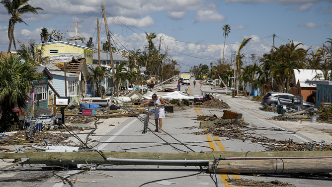 A resident walks past debris on Pine Island Road following Hurricane Ian in Matlacha Isles, Florida, US, on Saturday, Oct. 1, 2022. Research firm Enki Holdings LLC pegs the economic cost of Hurricane Ian at $60 billion to $70 billion, based on damage to homes and infrastructure, as well as the cost of reconstruction and longer-term knock-on effects including the disruption in tourism.