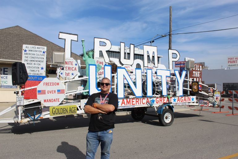 A demonstrator poses in front of a trailer adorned with pro-Trump slogans in Port Huron, Michigan