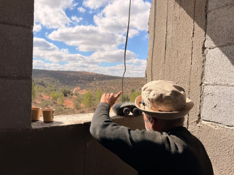 A Beita resident monitors an Israeli outpost on the opposite hill through binoculars. During the olive harvest, families keep someone on lookout in case settlers attack