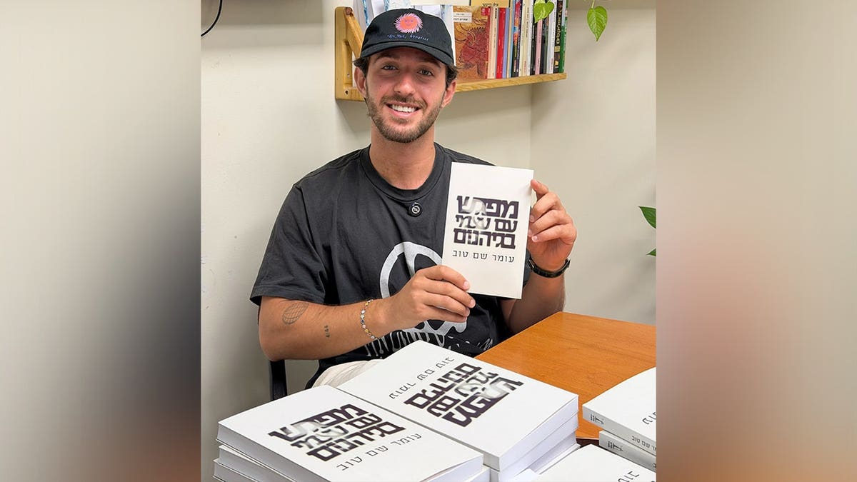 Omer Shem Tov holds up a copy of his book in Hebrew