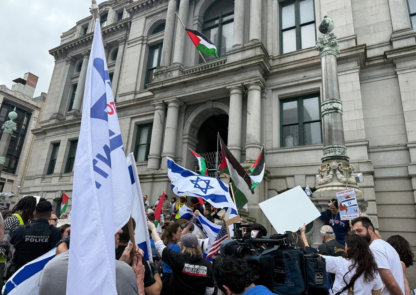 Counterprotesters waved Israeli flags on the sidewalk outside City Hall in 2025 as a Palestinian flag flew above.