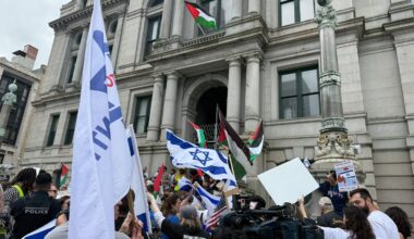 Counterprotesters waved Israeli flags on the sidewalk outside City Hall in 2025 as a Palestinian flag flew above.
