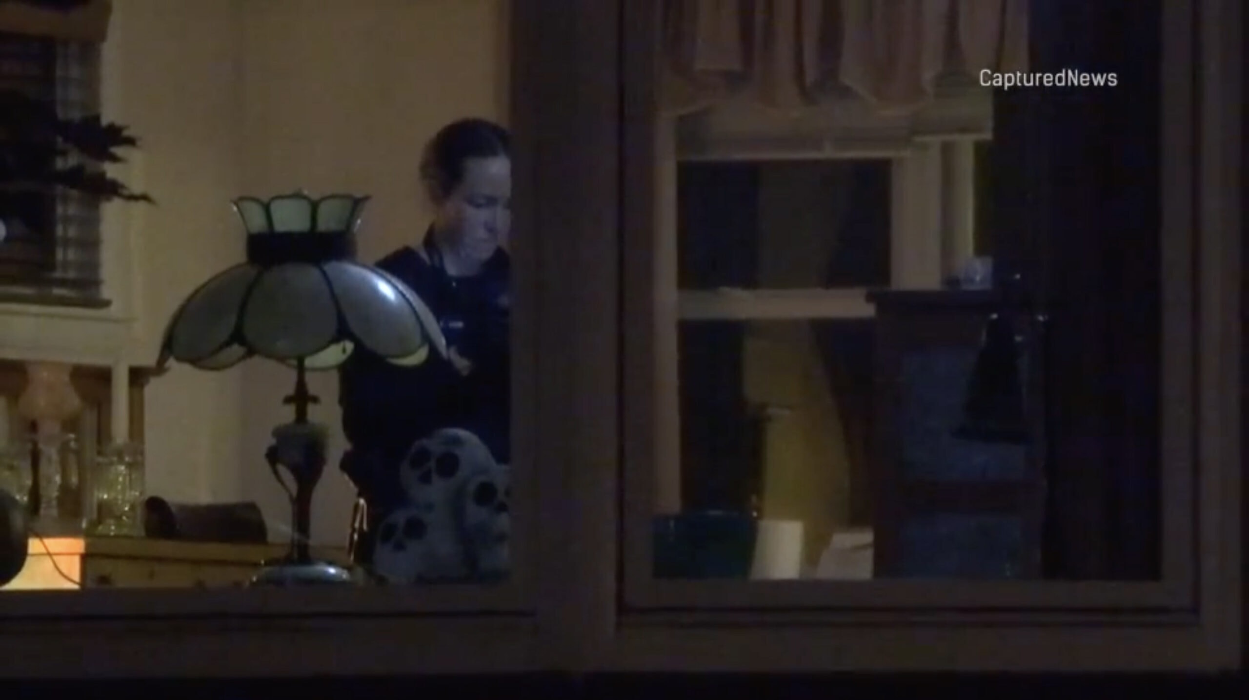 An investigator seen through a window working inside a home at night