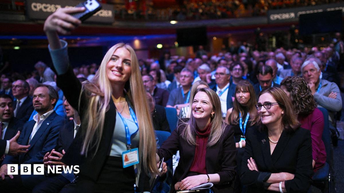A young woman with long blonde hair takes a selfie with shadow housing secretary Katie Lam, who is sitting in the conference hall with Tory members