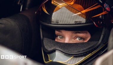 Swedish Top Fuel drag racing driver Susanne Callin wearing a black and orange racing helmet with just her eyes exposed through the visor, looking directly at the camera, taken at Mantorp in Sweden in 2025.