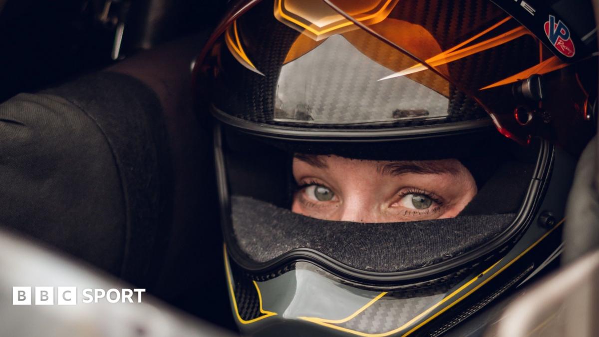 Swedish Top Fuel drag racing driver Susanne Callin wearing a black and orange racing helmet with just her eyes exposed through the visor, looking directly at the camera, taken at Mantorp in Sweden in 2025.