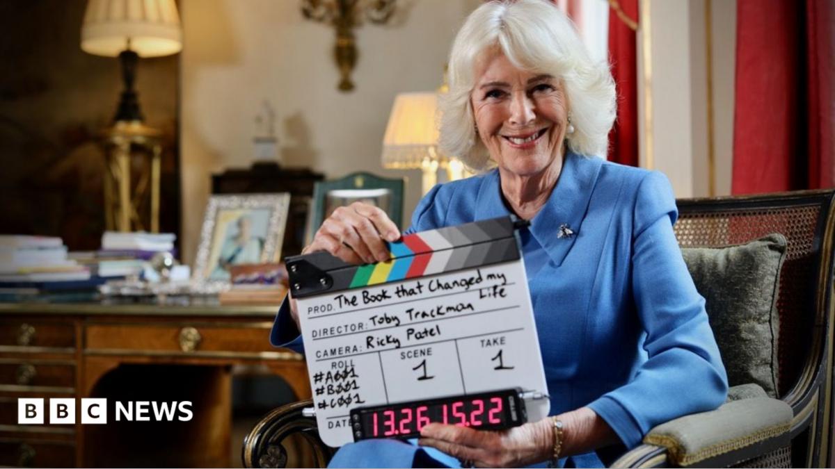 Queen Camilla sits in a chair reading a copy of William Boyd's Restless