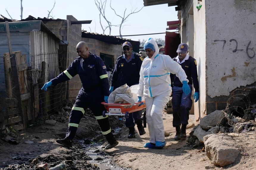 Police officers carry the body of a person on a stretcher after a mass shooting at an informal settlement in the Cleveland suburb of Johannesburg, South Africa, on June 10.