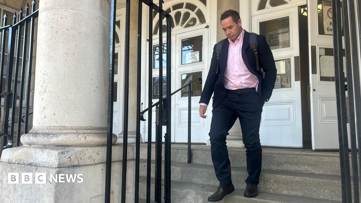 Kieran Hayler pictured leaving Lewes Crown Court on 5 October. Hayler, who is wearing a rucksack, is wearing a dark suit and pink shirt.