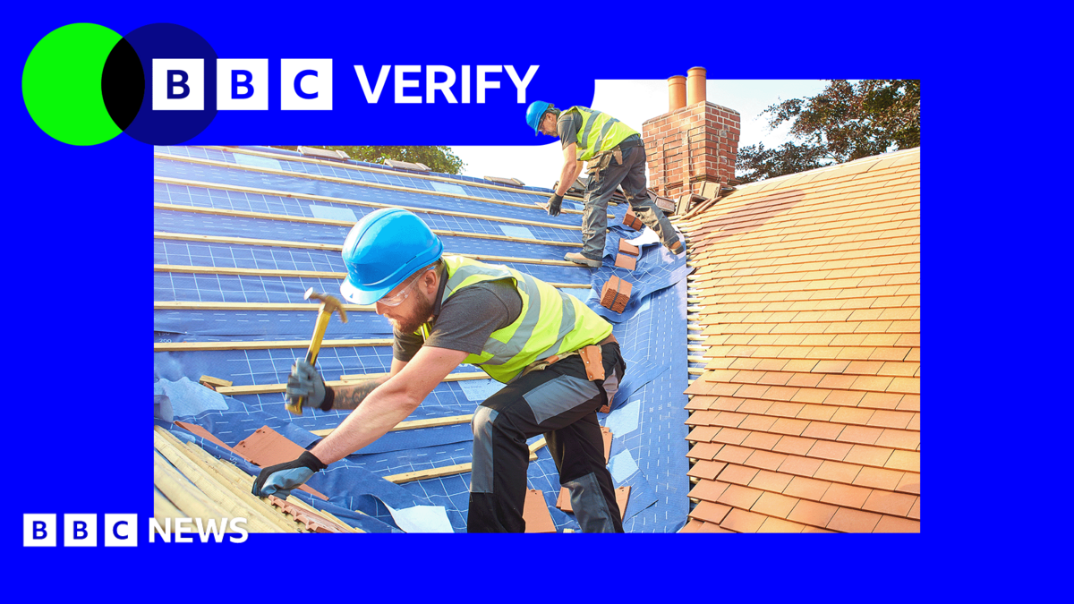 Two builders in blue hard hats and high-viz vests work on a new roof