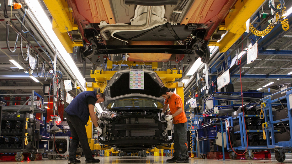 Men are seen working on a car at a Ford factory.