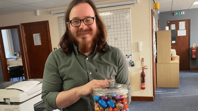 Joshua Kerry smiling while holding a glass jar of chocolate eggs.