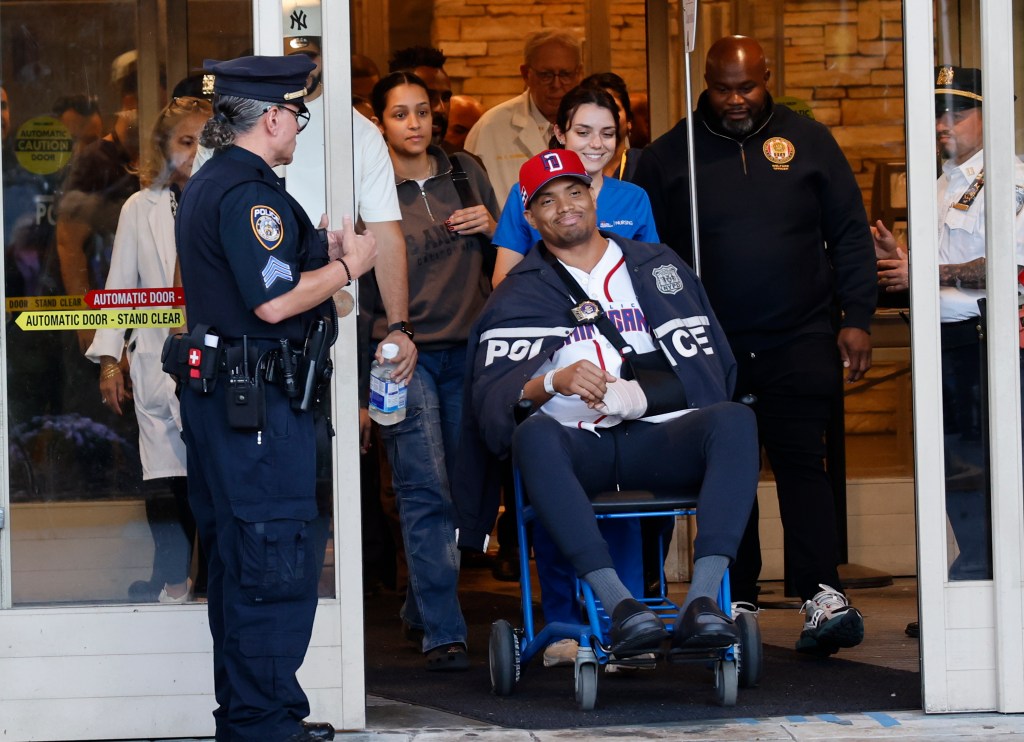 Detective Jose Mercedes leaves the hospital in a wheelchair, surrounded by police officers and hospital staff.