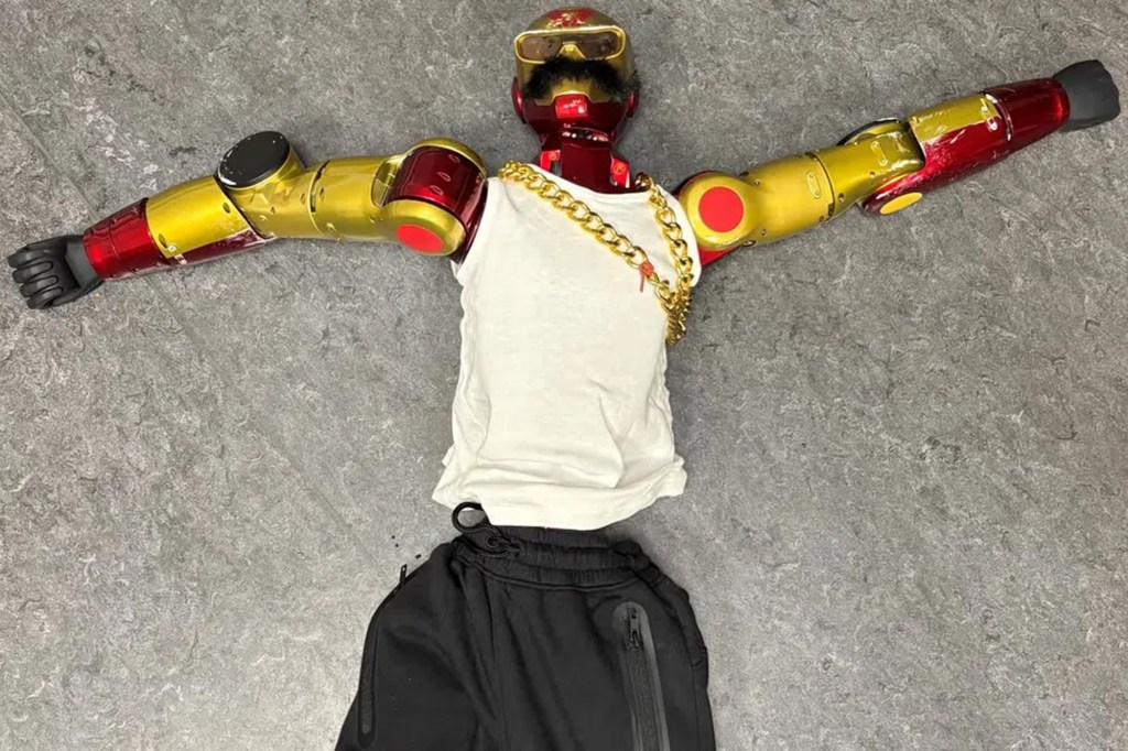 A red and gold robot lying flat on the floor, wearing a white tank top, gold chain necklace, and black sweatpants.
