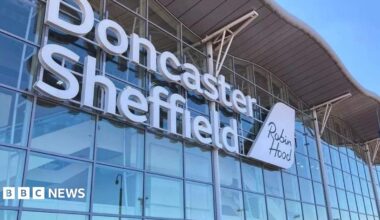 A wall made up of dozens of windows has large white lettering which says Doncaster Sheffield. There is a sign which looks like the tail of a plane saying Robin Hood.