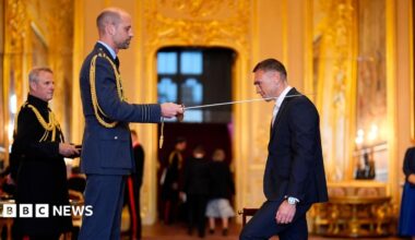 The Prince of Wales knights Sir Kevin Sinfield with a sword at an investiture in a grand, gold room at Windsor Castle.