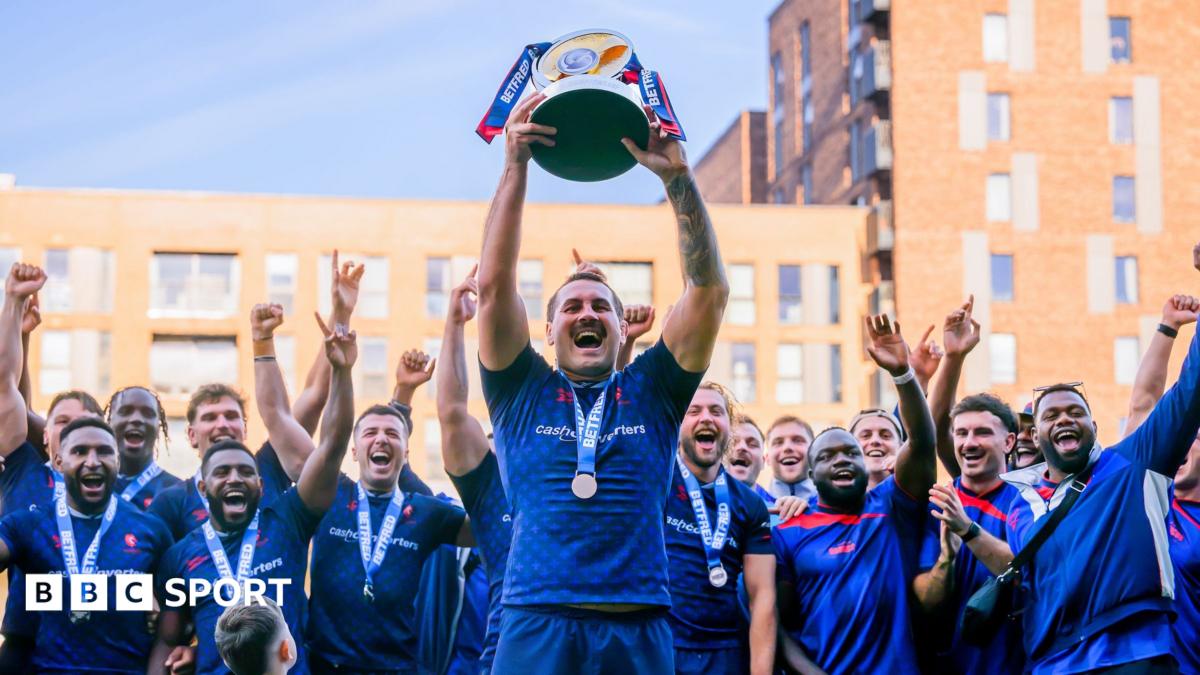 The captain of London Broncos lifts the Championship trophy as his team-mates lift their arms in celebration behind him