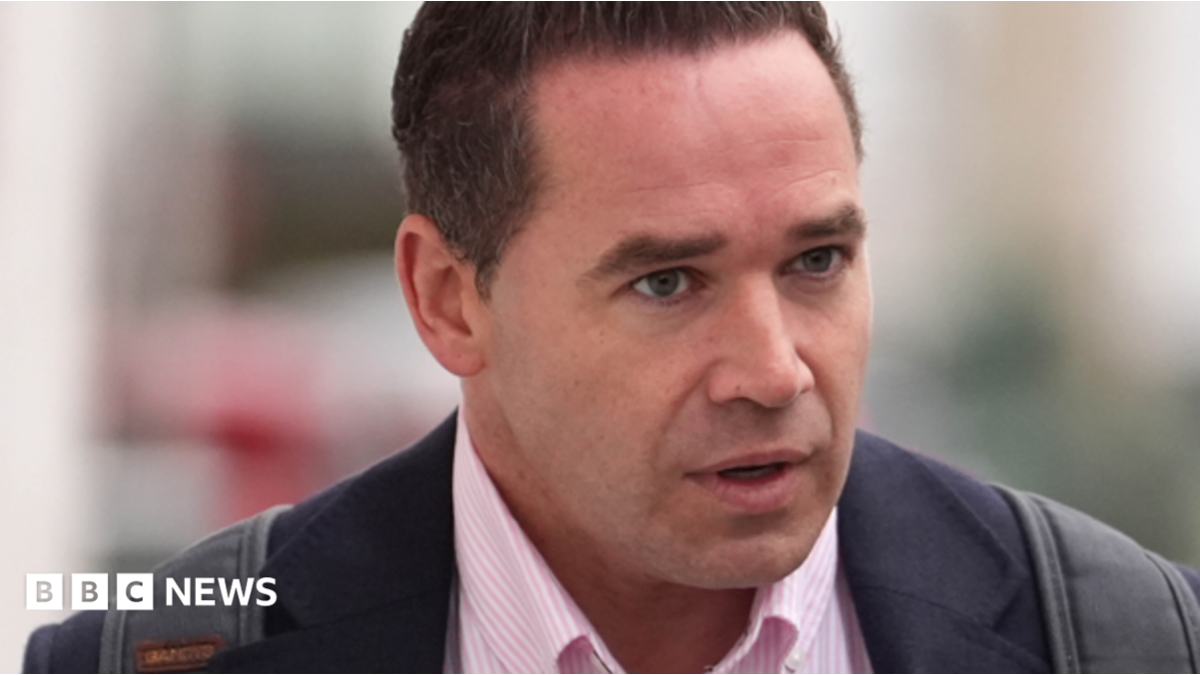 Kieran Hayler- a man wearing a pink shirt and suit jacket walking