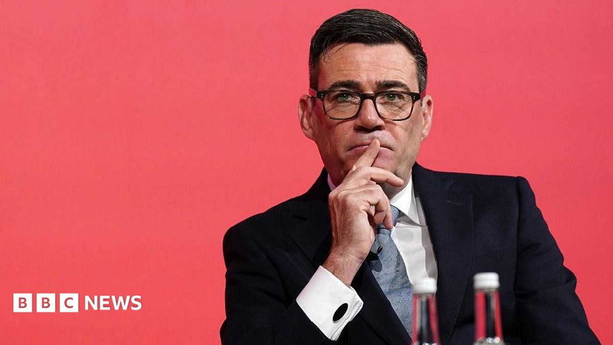 Andy Burnham looks pensive while sitting down with a red background.
