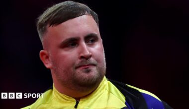 Luke Littler looking to his left in a yellow and blue darts top