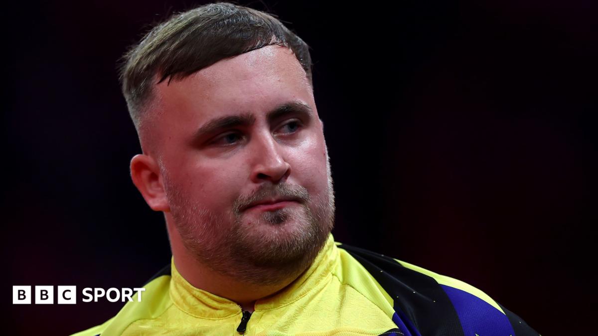 Luke Littler looking to his left in a yellow and blue darts top