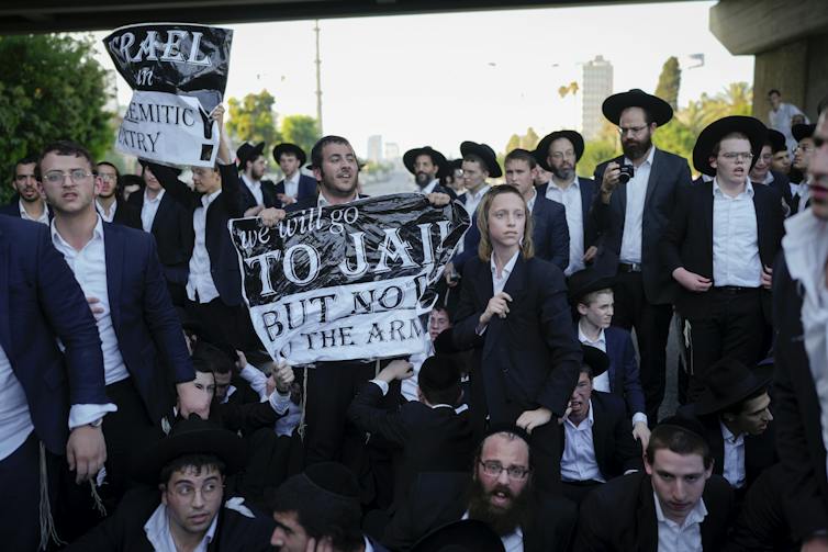 Men in black suits and white shirts hold signs that say, 'We will go to jail, but not to the army.'