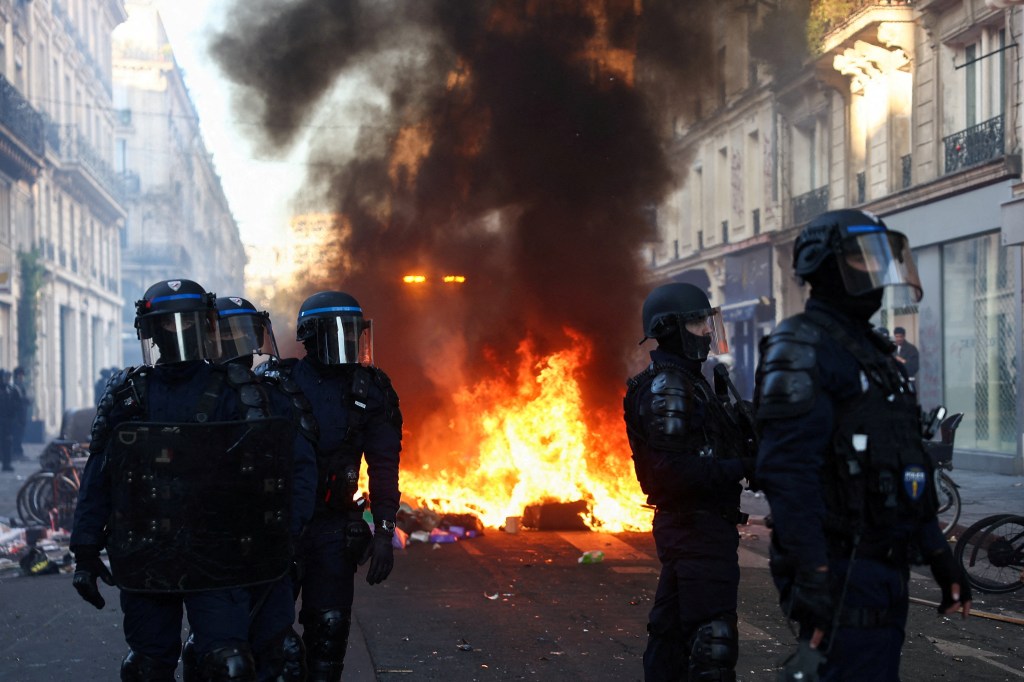 Police officers in riot gear stand guard as a fire burns during civil unrest in Paris.