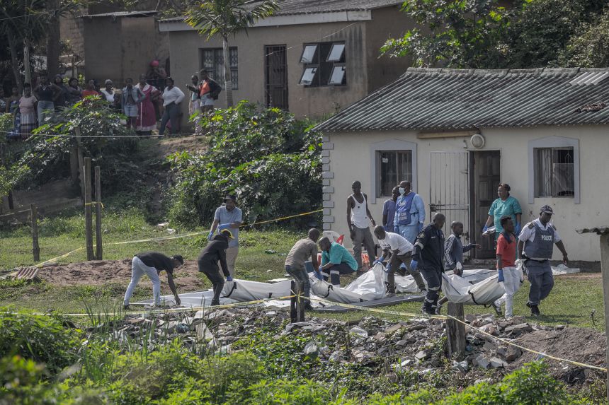 South African forensic pathology personnel are assisted by community members to carry the body of a victim, following a mass shooting in the Ziko area of KwaMakhutha, on September 23.