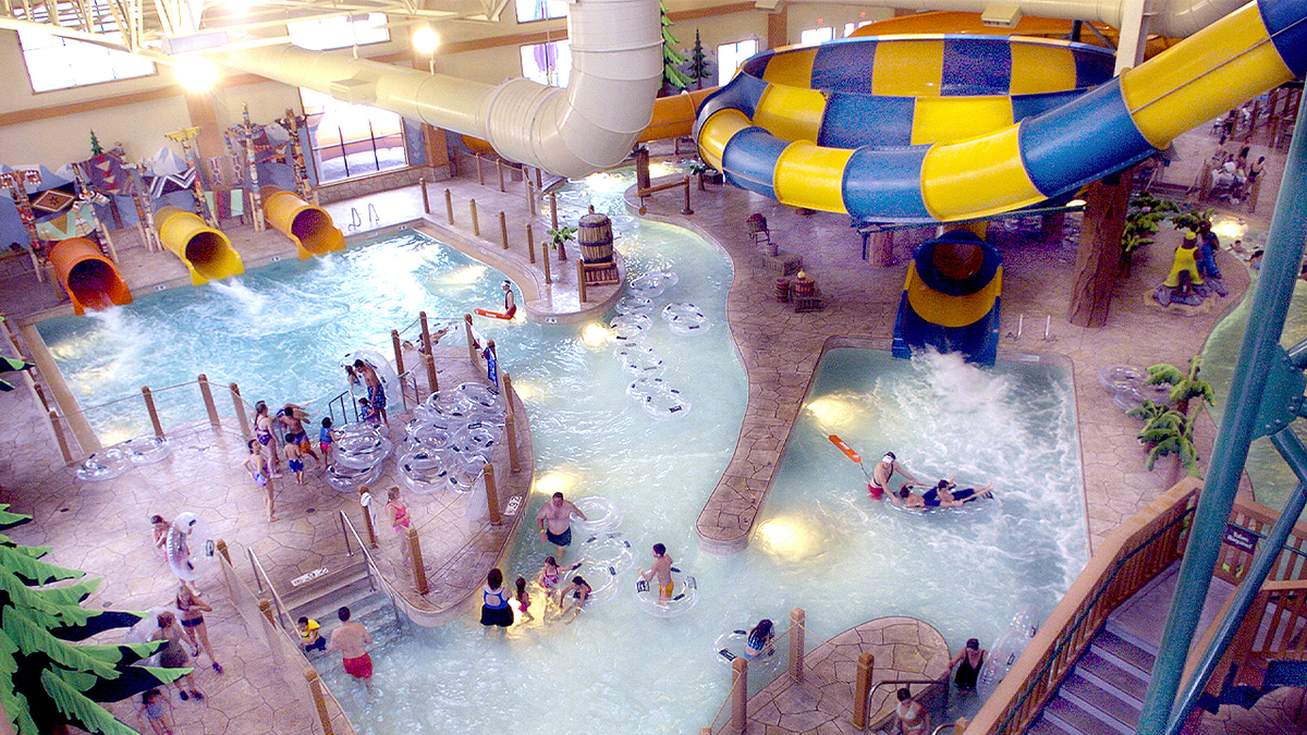 Guests swim and ride inner tubes beneath colorful slides at an indoor water park