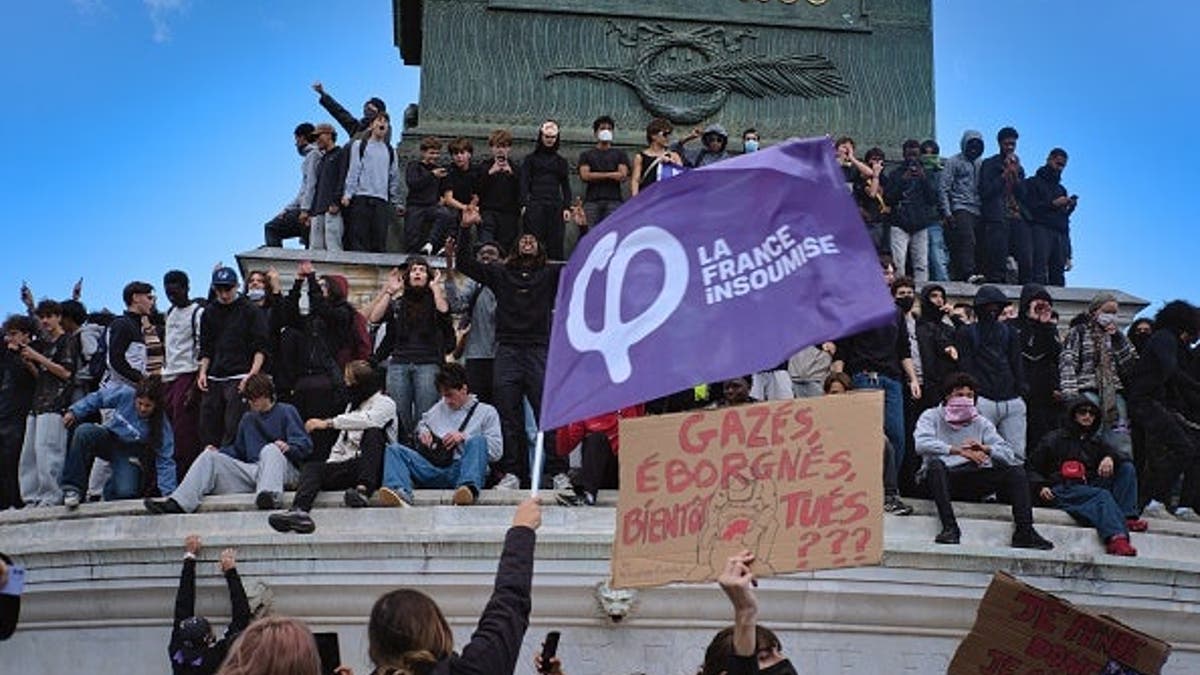 High school students gather at Place de la Bastille in Paris, one waving an LFI flag.