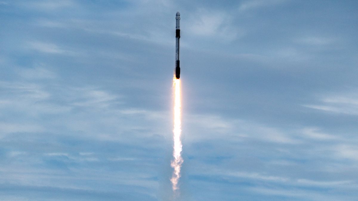A SpaceX Falcon 9 rocket l;aunches into a blue sky with light clouds